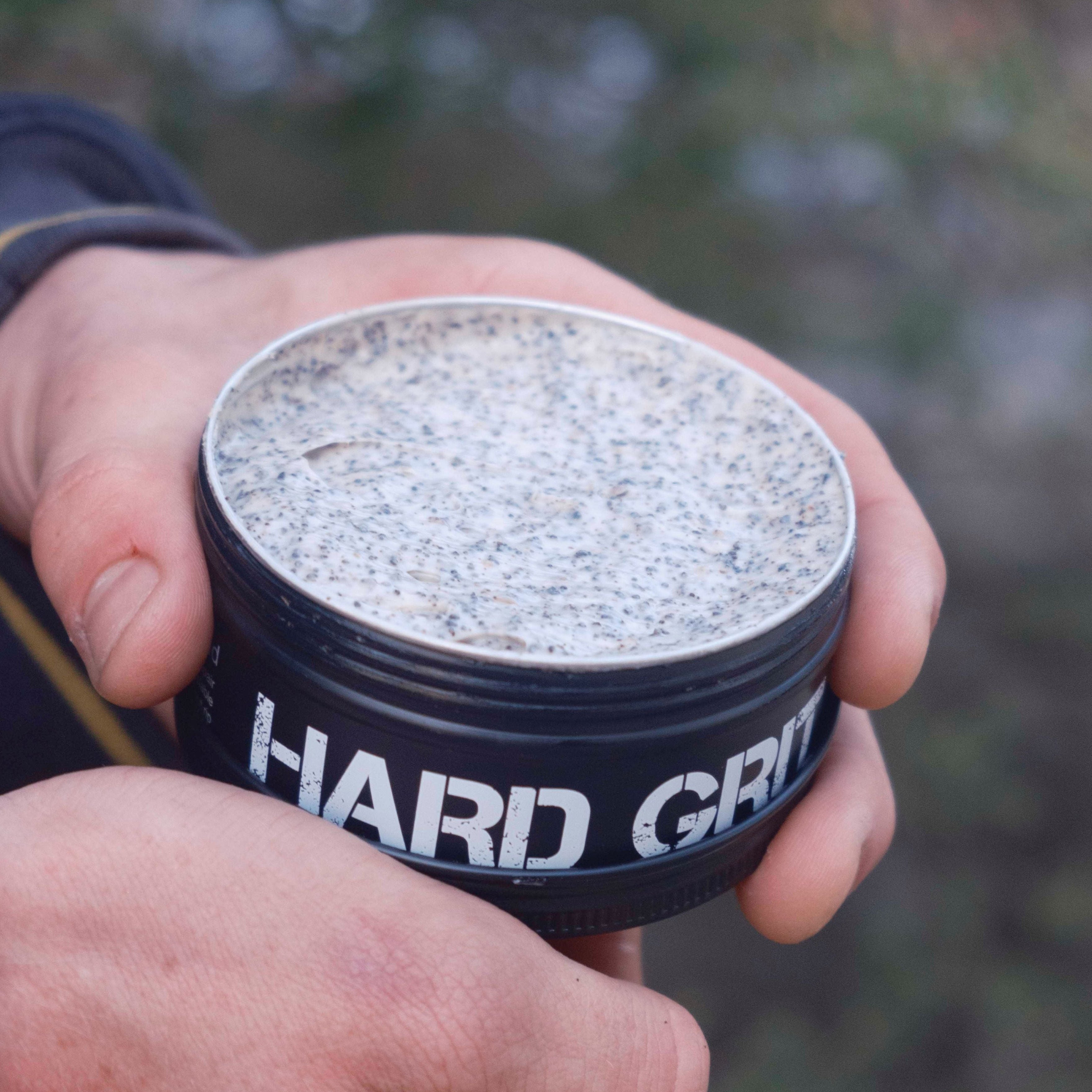 Person holding a container labeled 'Hard Grit' outdoors