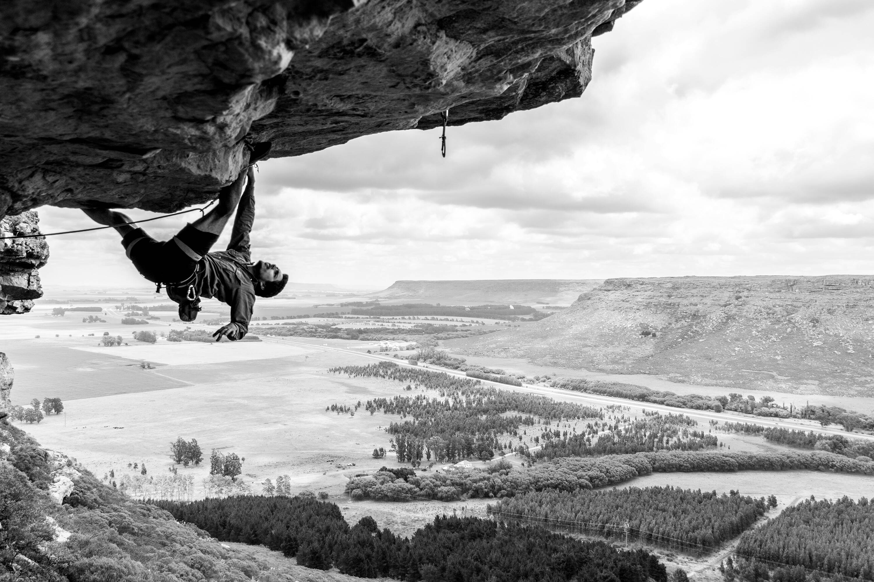 Person rock climbing on a cliff edge with a scenic landscape below