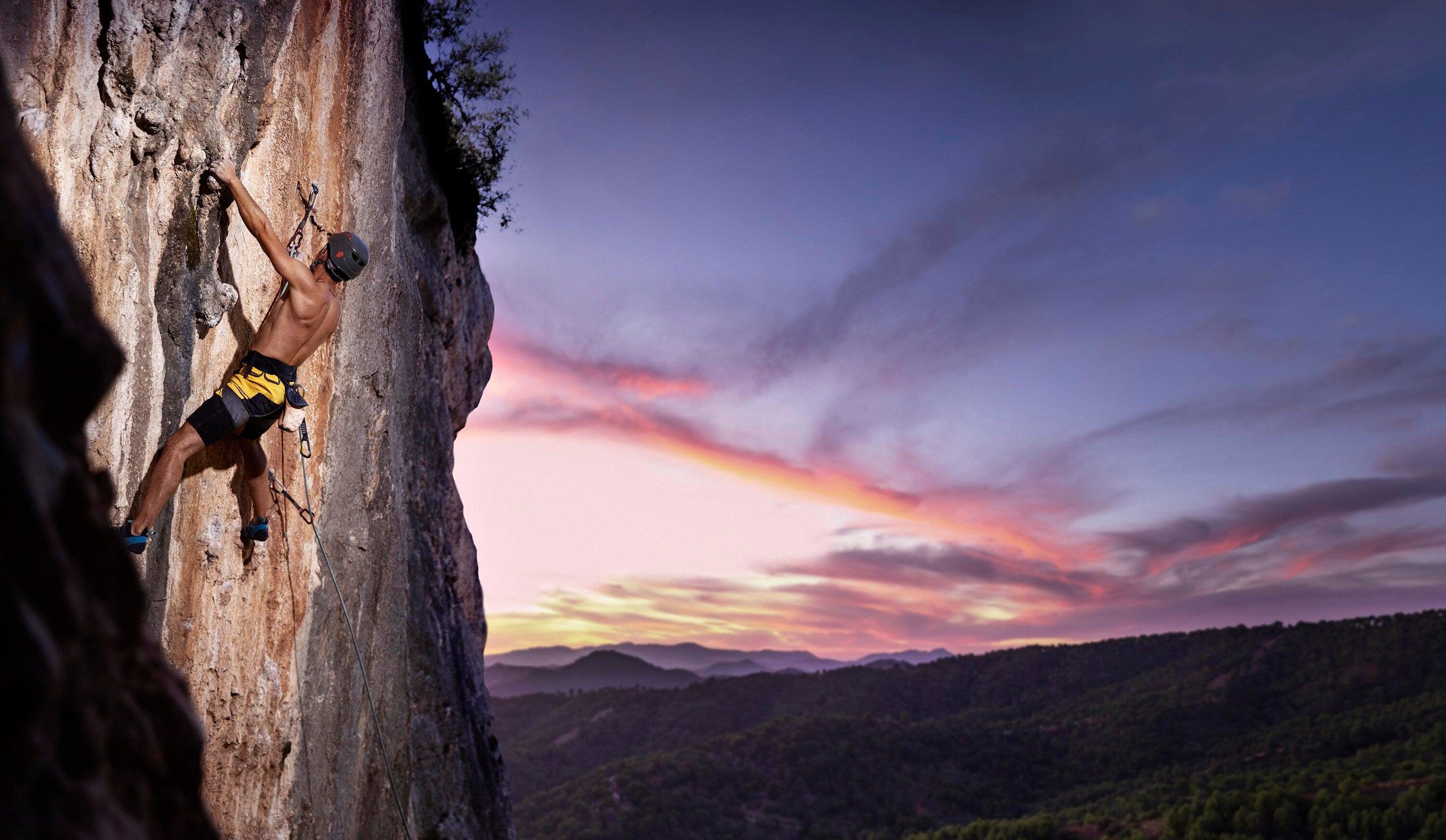 Person climbing a rock face with a colorful sunset in the background