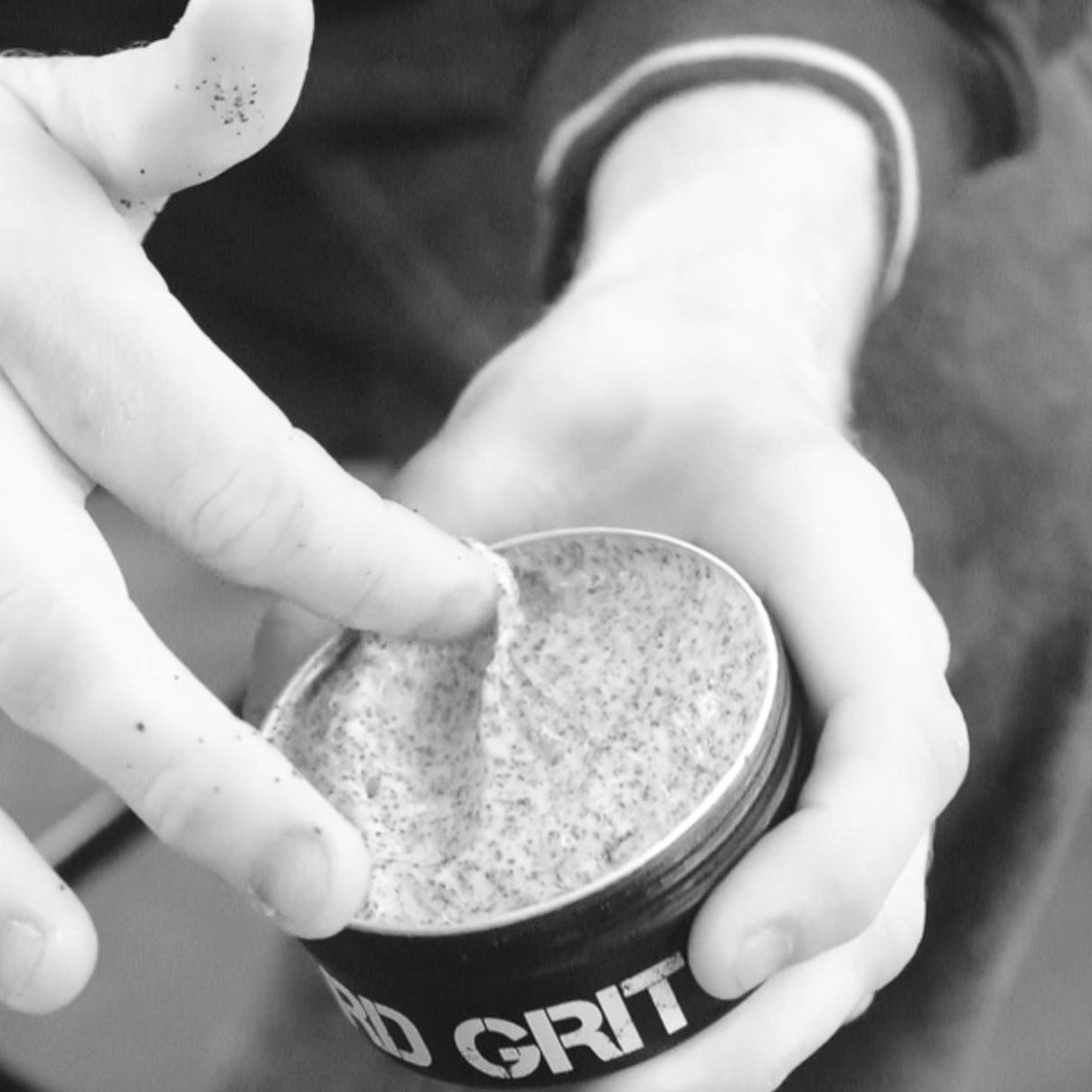 Hand removing Hard Grit cream from open tin loaded with coconut husk exfoliant which can be seen in the cream