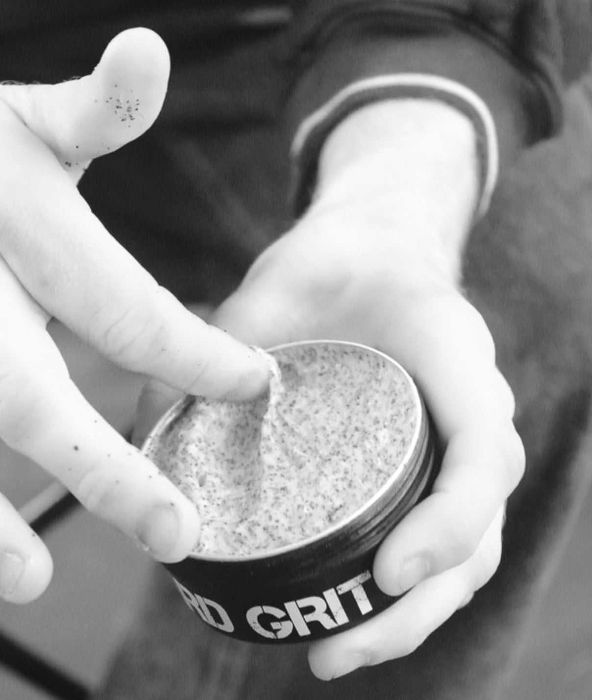Hand removing Hard Grit cream from open tin loaded with coconut husk exfoliant which can be seen in the cream