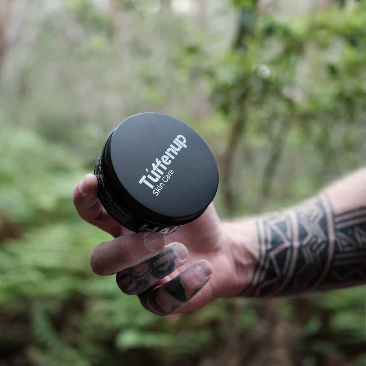 Hand holding 150ml aluminium tin of Tuffenup's HARD GRIT, containing crushed coconut exfoliant set in a high quality hand cream to remove dead skin, grease, grime, dirt, and condition the remaining healthy skin to get you back climbing fast.

Against a blurred natural background